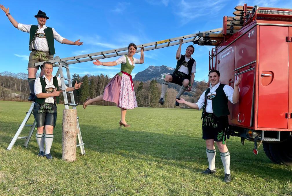 Elbach feiert den Brass Freida und Bavarian Ninja im Festzelt Elbach. Gruppe von jungen Trachtler aus Elbach stehen vor altem Feuerwehrauto und schwingen sich an einer Leiter entlang. Sie symbolisieren das Event "Bavarian Ninja".